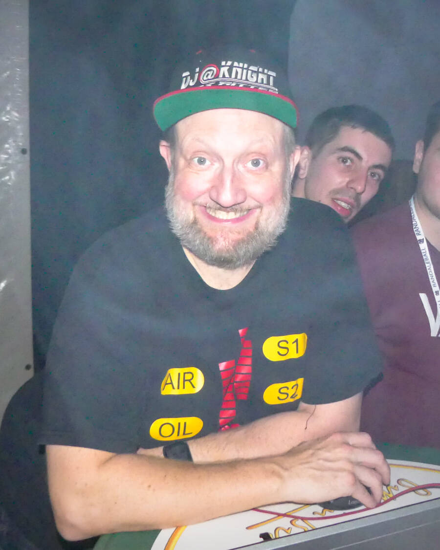 DJ mit Cap am Pult mit Notebook im Nebel, umgeben von G&auml;sten