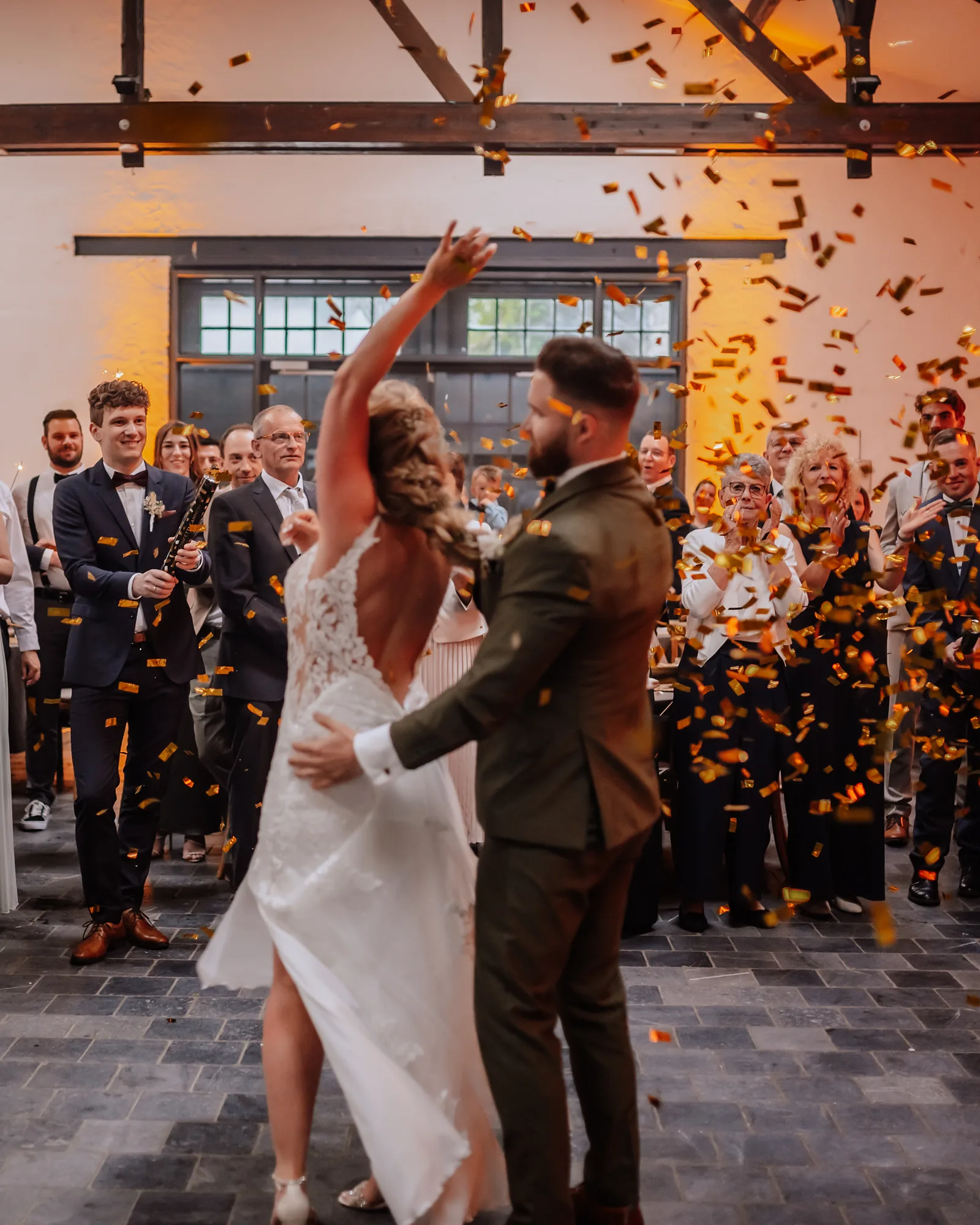 Brautpaar beim Hochzeitstanz im Konfettiregen, die Braut rei&szlig;t den Arm hoch, ringsum feiern die Hochzeitsg&auml;ste.