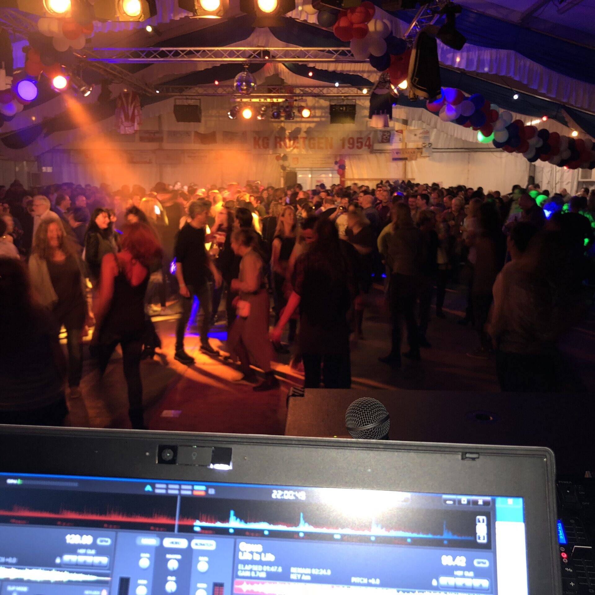 Volle Tanzfl&auml;che im Festzelt in orangem Licht, vorn der Notebook-Bildschirm am DJ-Pult, hinten das Banner der KG Roetgen